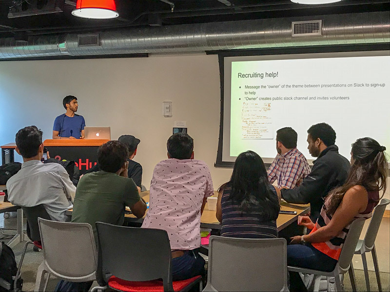 Photo of a person presenting at a podium and others watching