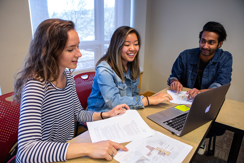 Photo of students sitting around a table with papers and a computer