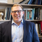 Photo of Vince Slaugh standing in front of a bookshelf smiling