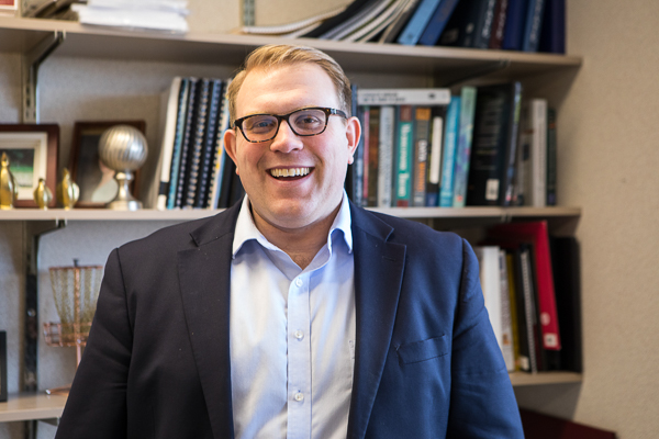 Photo of Vince Slaugh standing in front of a bookshelf smiling