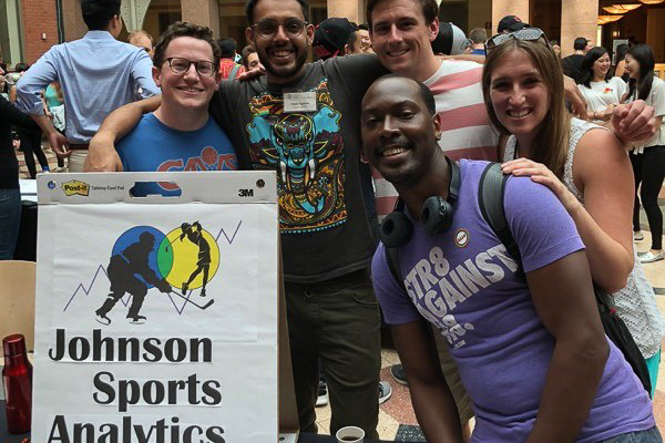 Students stand next to their Johnson Sport Analytics Club sign