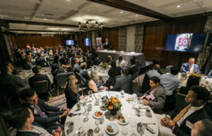 Guests sit around tables and listen to a speaker