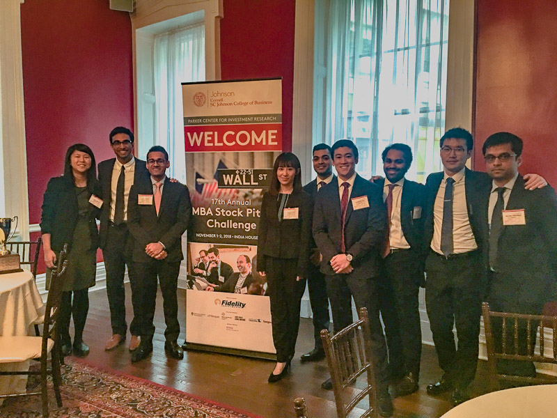 Several students stand in front of the MBA stock pitch challenge sign