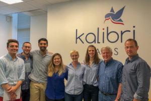 Eight people stand in front of a wall that says Kalibri Labs