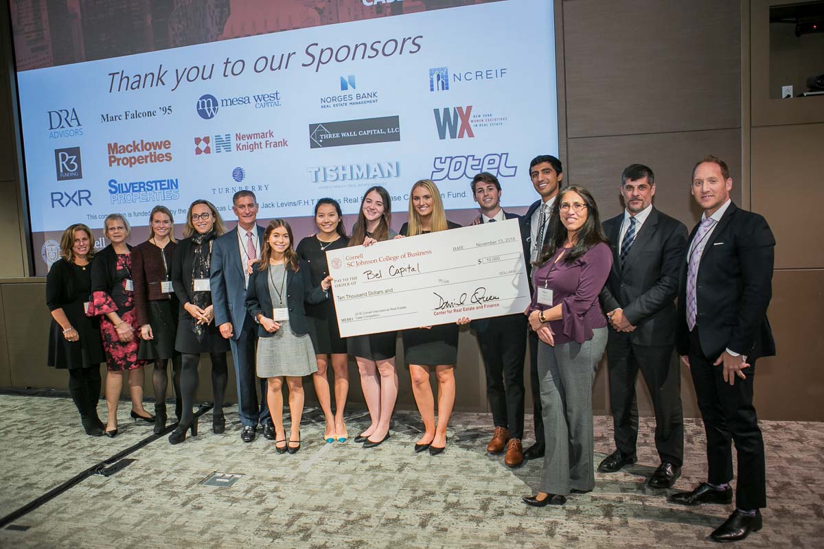 A large group stands with an oversized check