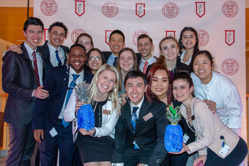 A group of students in front of the HEC backdrop holding pineapples