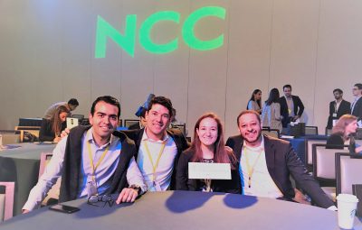 Four students sitting at a table with NCC in the background