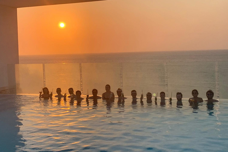 Students drinking cocktails in a pool with a sunset background