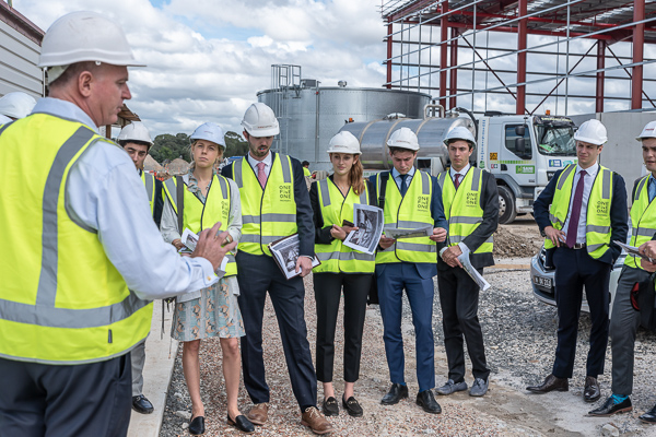 A group stands with construction hats and gear touring a site