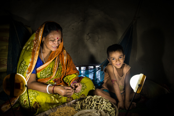 A woman and child sit next to a solar lamp in a tent