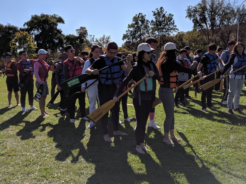 Students standing on land holding oars 