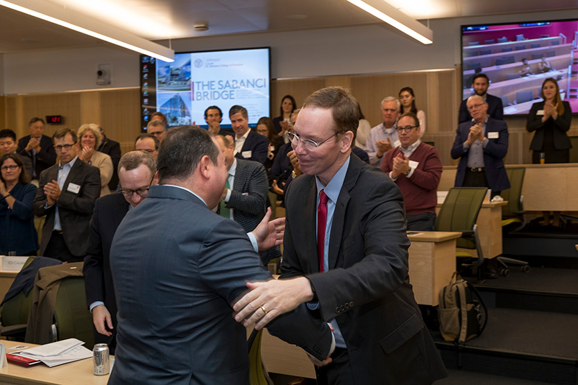 Dean Mark Nelson shaking hands with Demir Sabanci, MBA ’99, at the Sabanci Bridge dedication, Oct. 21, 2019. Members of the Johnson Advisory Council are seated in the background.