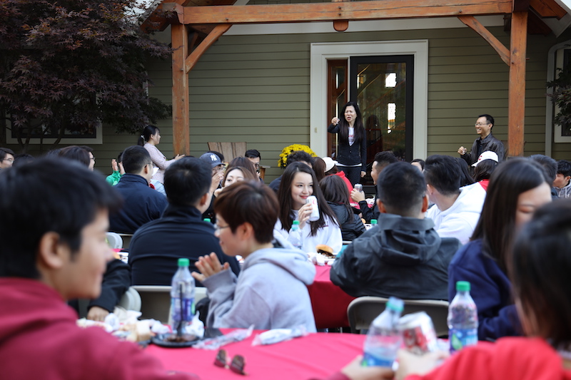 Ya Ru speaks to students seated at tables in her yard 