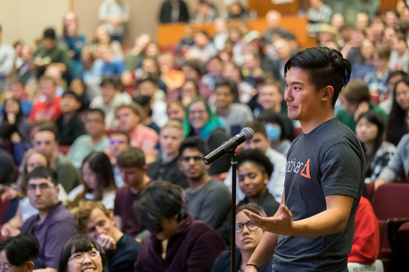 A packed auditorium with a student asking a question