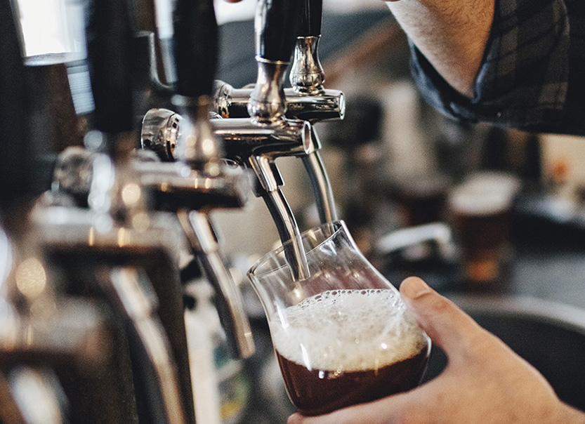 Hand holding a glass and pouring beer in a row of beer taps.