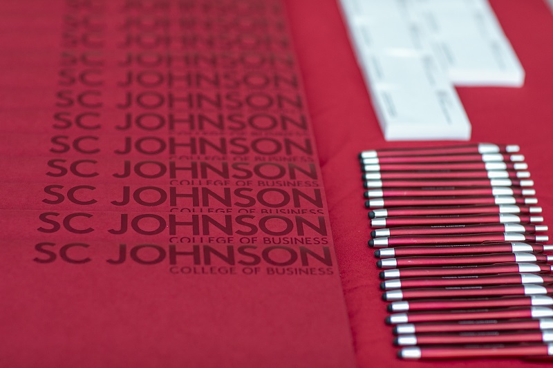 Pens, folders, and small note pads with the SC Johnson College of Business logo lie on a table.