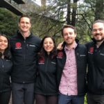 Five students pose for a photo wearing branded jackets.