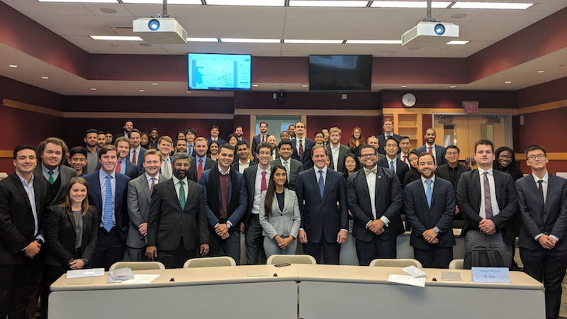 A large group of students and a speaker pose for a photo in a lecture hall