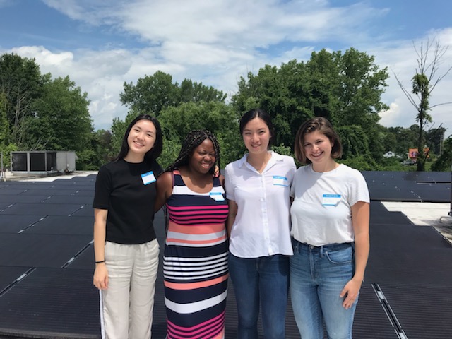 Four women standing on top of solar panels on a roof.