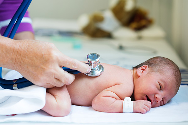 doctor's hand holding a stethoscope and listening to hearbeat of cute newborn baby