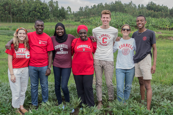 A group of people wearing Cornell attire pose in a field