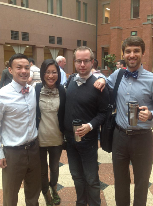 Four former students pose on campus, all wearing bow ties.