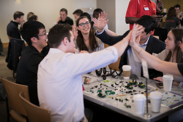 Students high-five over a table of LEGO