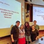 Executive MBA students and senior lecturer Casanova stand in front of a presentation board for the class