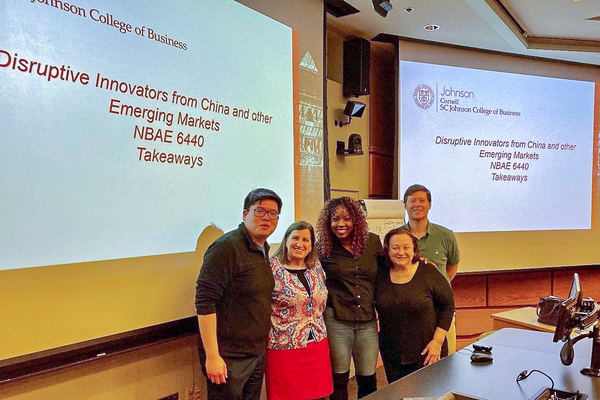 Executive MBA students and senior lecturer Casanova stand in front of a presentation board for the class