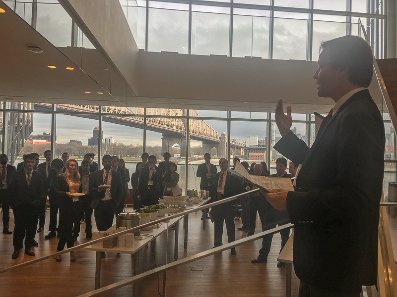 Scott speaking to a large reception with the NYC skyline outside of the window