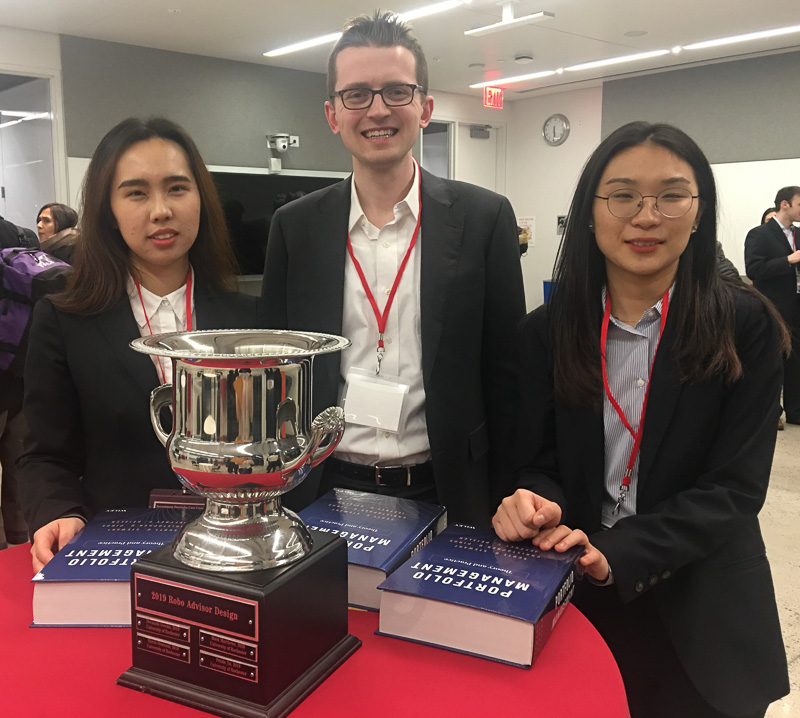 Three students pose with a large trophy and three big textbooks