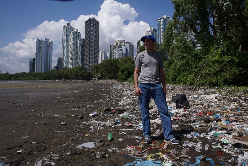 Fisk standing on a plastic-strewn beach with a skyline in the background