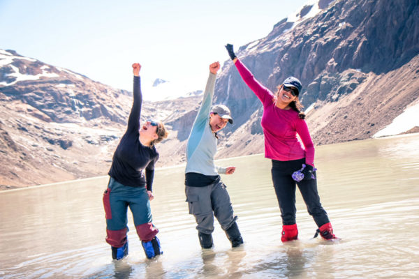 Three students stand in knee-deep water in Patagonia holding one of their fists in the air.