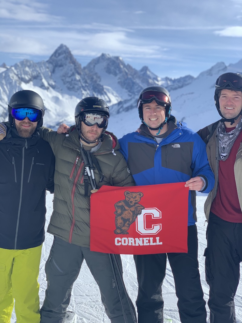 Four MBA students hold a Cornell banner in a posed photo at a ski resort.