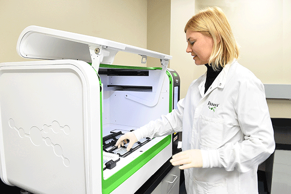 A scientist loads a Rheonix CARD cartridge onto the Encompass MDx workstation