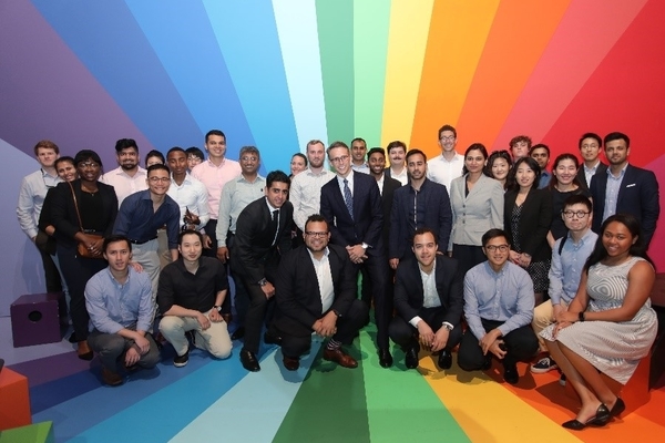 A large group of students stands in front of a rainbow colored wall