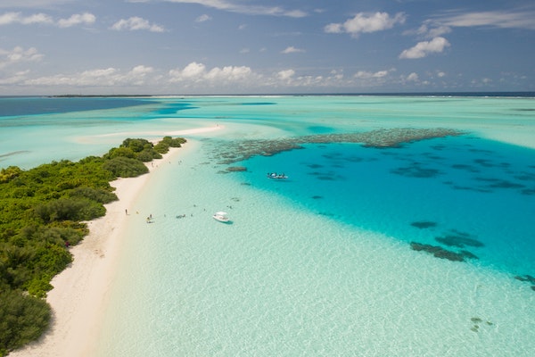 erial photo of a tropical island with a few anchored boats and people standing on the beach.