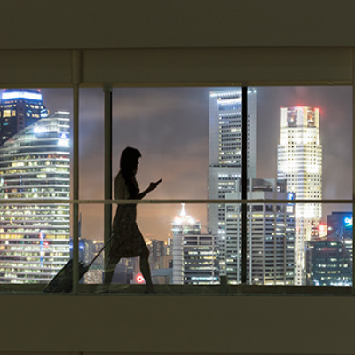 Woman walking while looking at her phone with cityscape in background