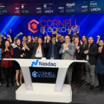 Group photo of Cornell Blockchain members cheering and standing behind the Nasdaq podium at the opening bell, with Cornell Blockchain on the wall behind them and on the podium in front of them