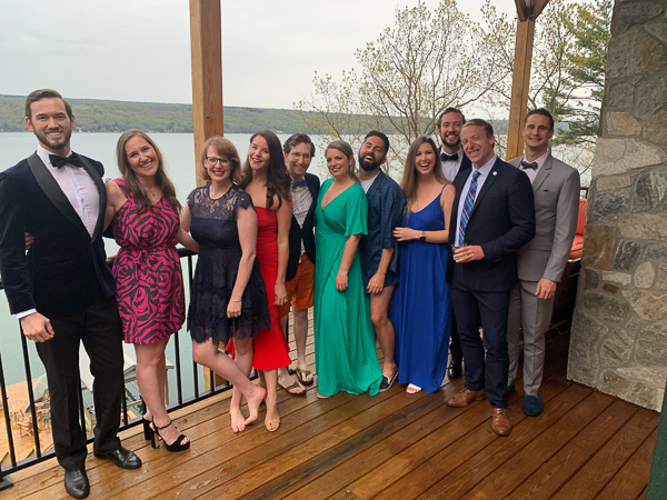 A group of 11 MBA students and partners wearing formal wear pose with a view Lake Cayuga behind them.