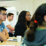 Side view of seated students looking toward the front of a classroom