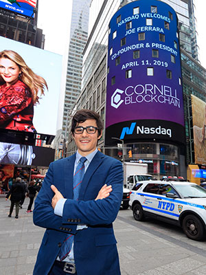 Joe Ferrara '19 standing outside Nasdaq in NYC with her name and Cornell Blockchain on the digital signage