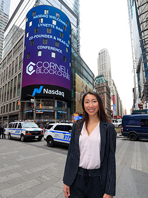 Lynette Ban ’19 standing outside Nasdaq in NYC with her name and Cornell Blockchain on the digital signage