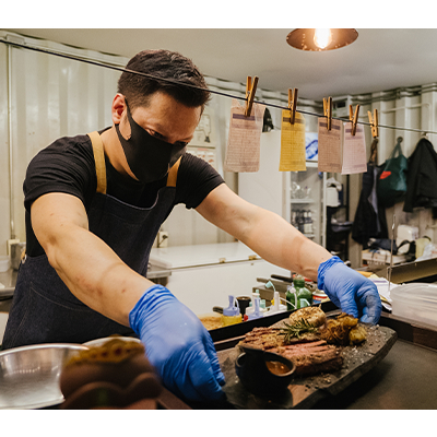 Man in a mask and gloves preparing orders in a kitchen