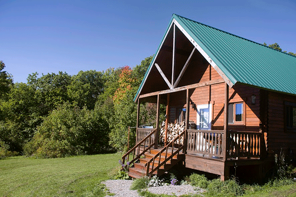 Photo of a cabin in a field with trees in the back