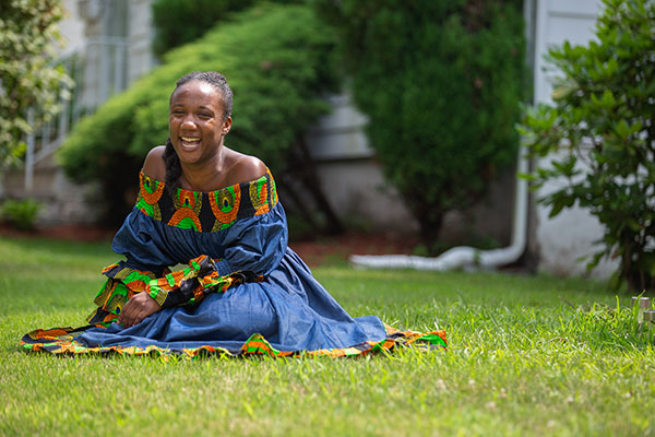 Kamillah Knight sitting on the grass and smiling, wearing a dress