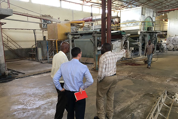 several men in a factory, on point to large equipment in the background