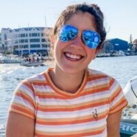 The author smiles for a picture, wearing sunglasses on a dock by the water.