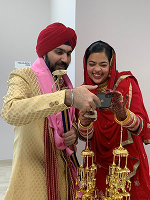 Harkiran Sodhi and her husband in Indian wedding attire holding and o=looking at a cell phone and smiling