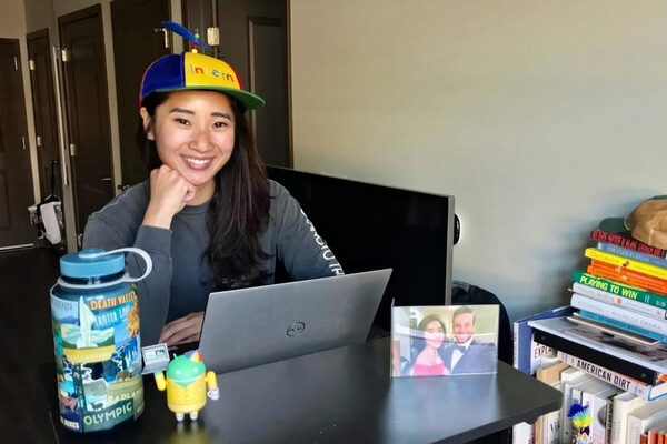 Taylor Nguyen sitting at her desk wearing a yellow and blue propeller hat that says intern.